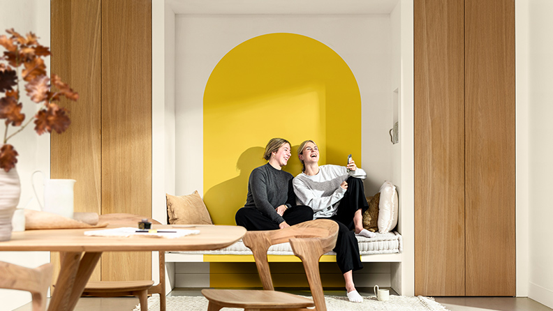 一对密友并肩坐在餐厅的长凳上。在她们身后是使用“金盏黄”涂刷的拱门图形。