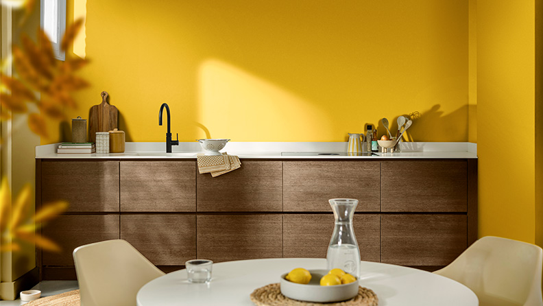 以“金盏黄”墙面和原木橱柜装点的现代厨房内，一系列简约设计的家居摆件，沐浴在自然光中。