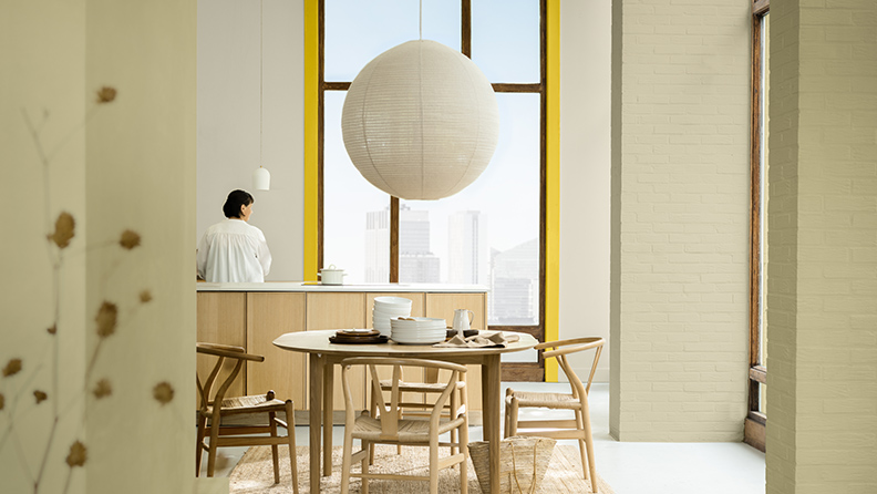 一位女士静立在一间开放式起居空间。一盏吊灯悬挂于屋顶，窗户四周是由“金盏黄”描绘的彩色框架。