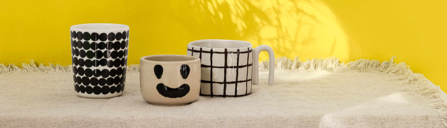 涂刷金盏黄的主题墙前面，放着三只咖啡杯，其中一只的杯身上有一个笑脸。