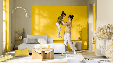 在一个现代起居空间里，妈妈抱起孩子。在她们身后是一面涂刷金盏黄的主题墙。